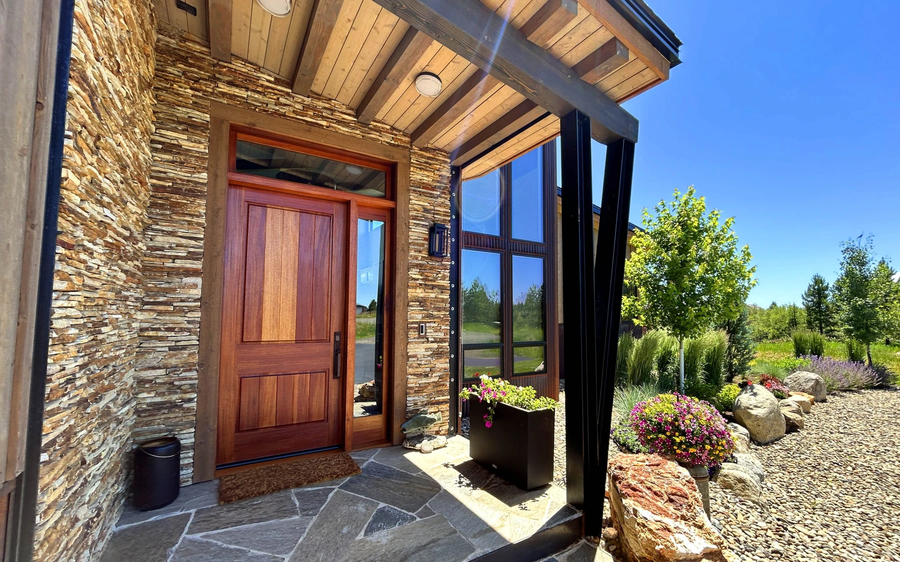 Exterior of the Contemporary Hideaway custom home near McCall, showing wood siding and timber details, stonework, and large windows.