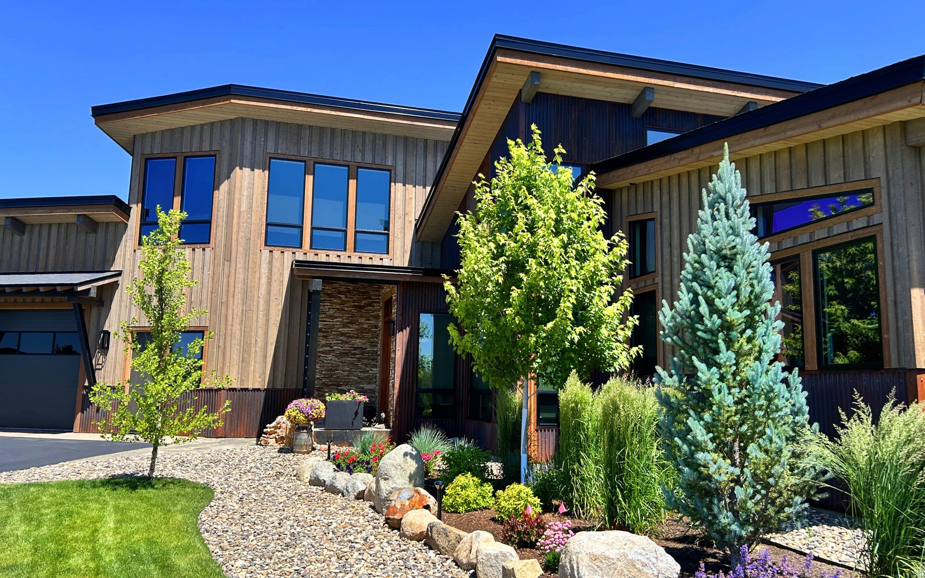 Exterior of the Contemporary Hideaway custom home near McCall, showing wood siding and timber details, stonework, and large windows.