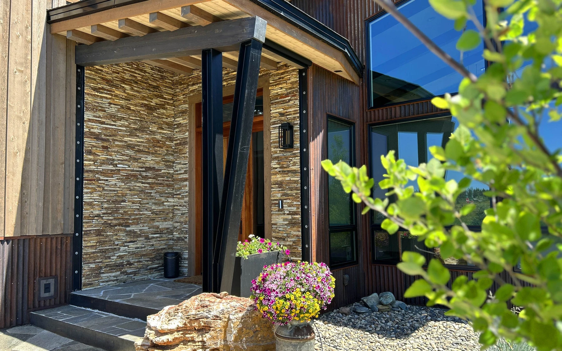 Exterior of the Contemporary Hideaway custom home near McCall, showing wood siding and timber details, stonework, and large windows.