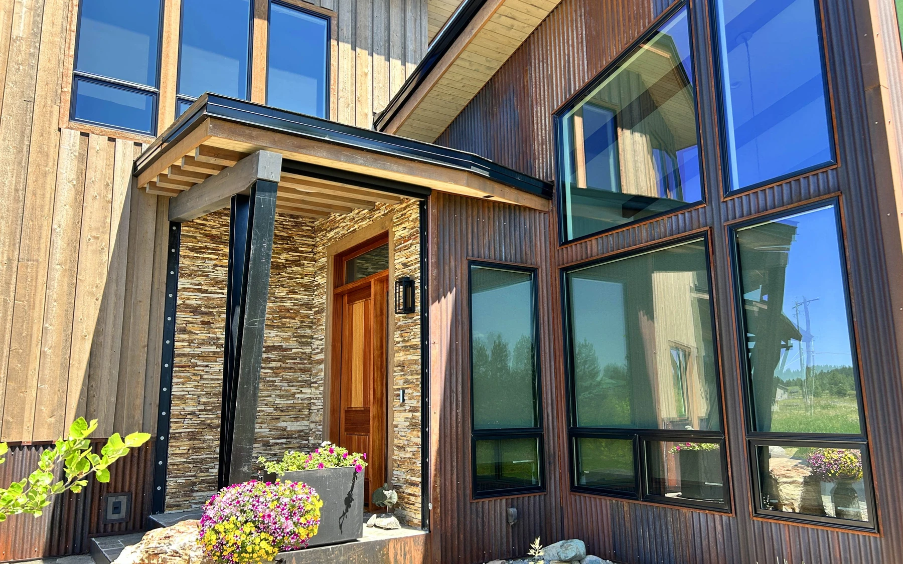 Exterior of the Contemporary Hideaway custom home near McCall, showing wood siding and timber details, stonework, and large windows.