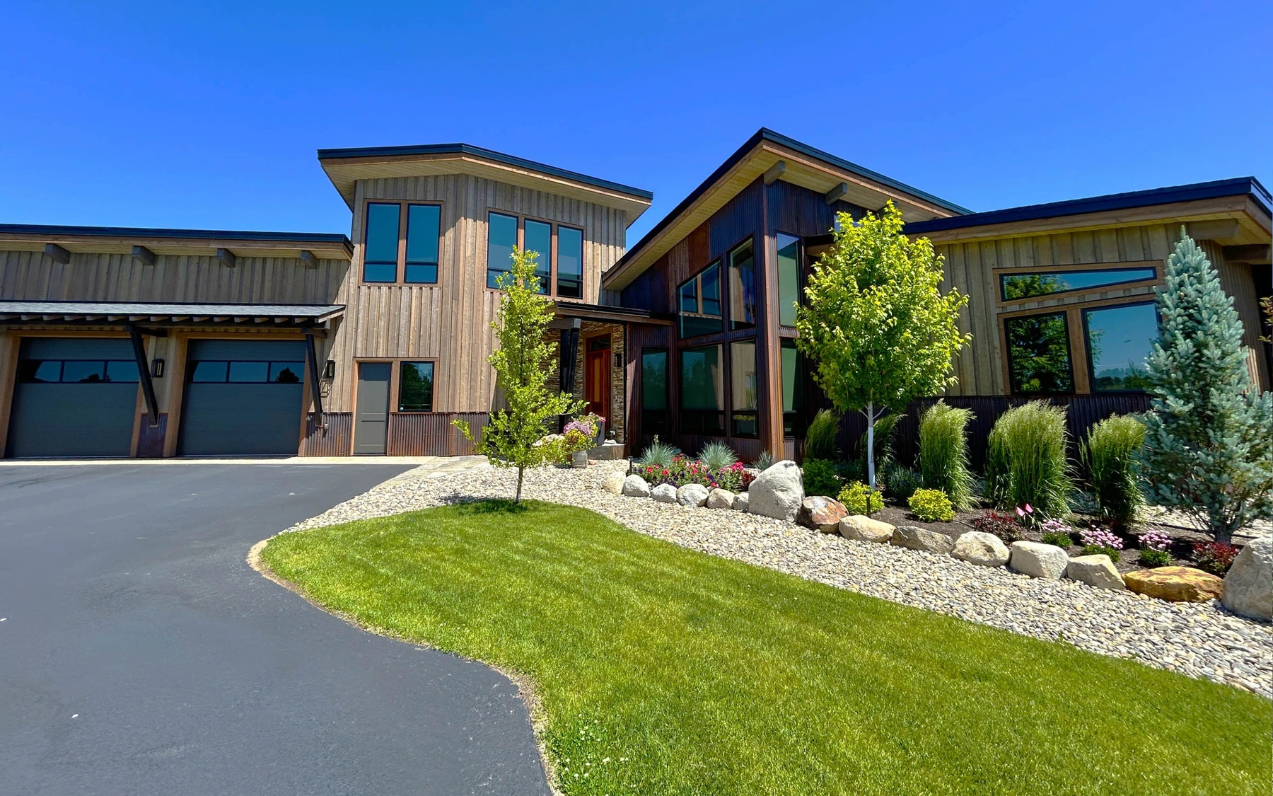 Garage approach at the Contemporary Hideaway custom home near McCall, with an attached garage, a broad driveway, and stone exterior details.