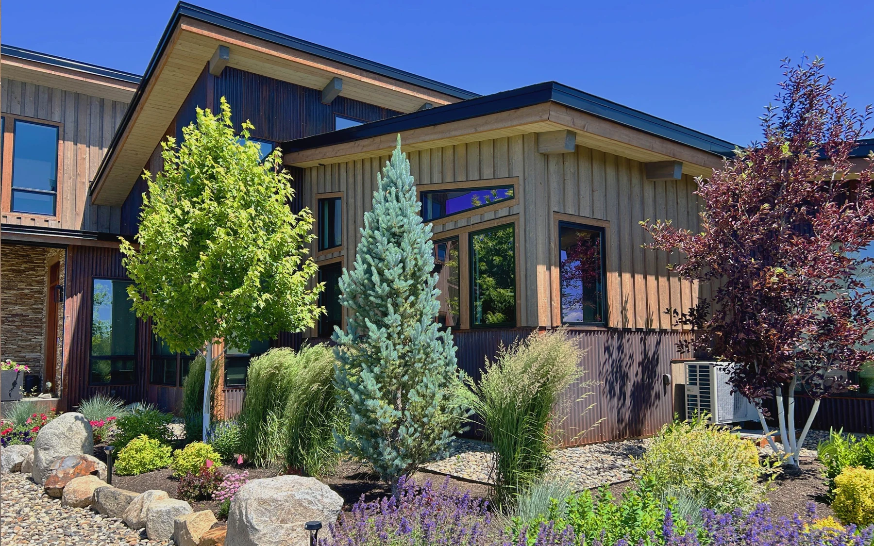 Exterior of the Contemporary Hideaway custom home near McCall, showing stonework, large windows, and the surrounding forest.