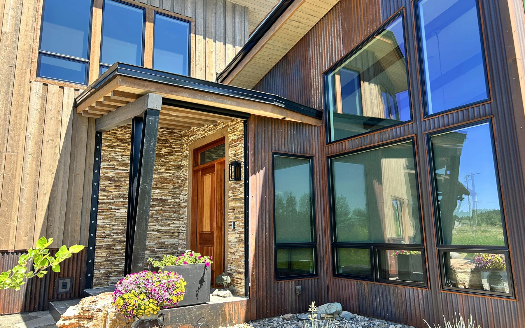 Exterior of the Contemporary Hideaway custom home near McCall, showing wood siding and timber details, stonework, and large windows.