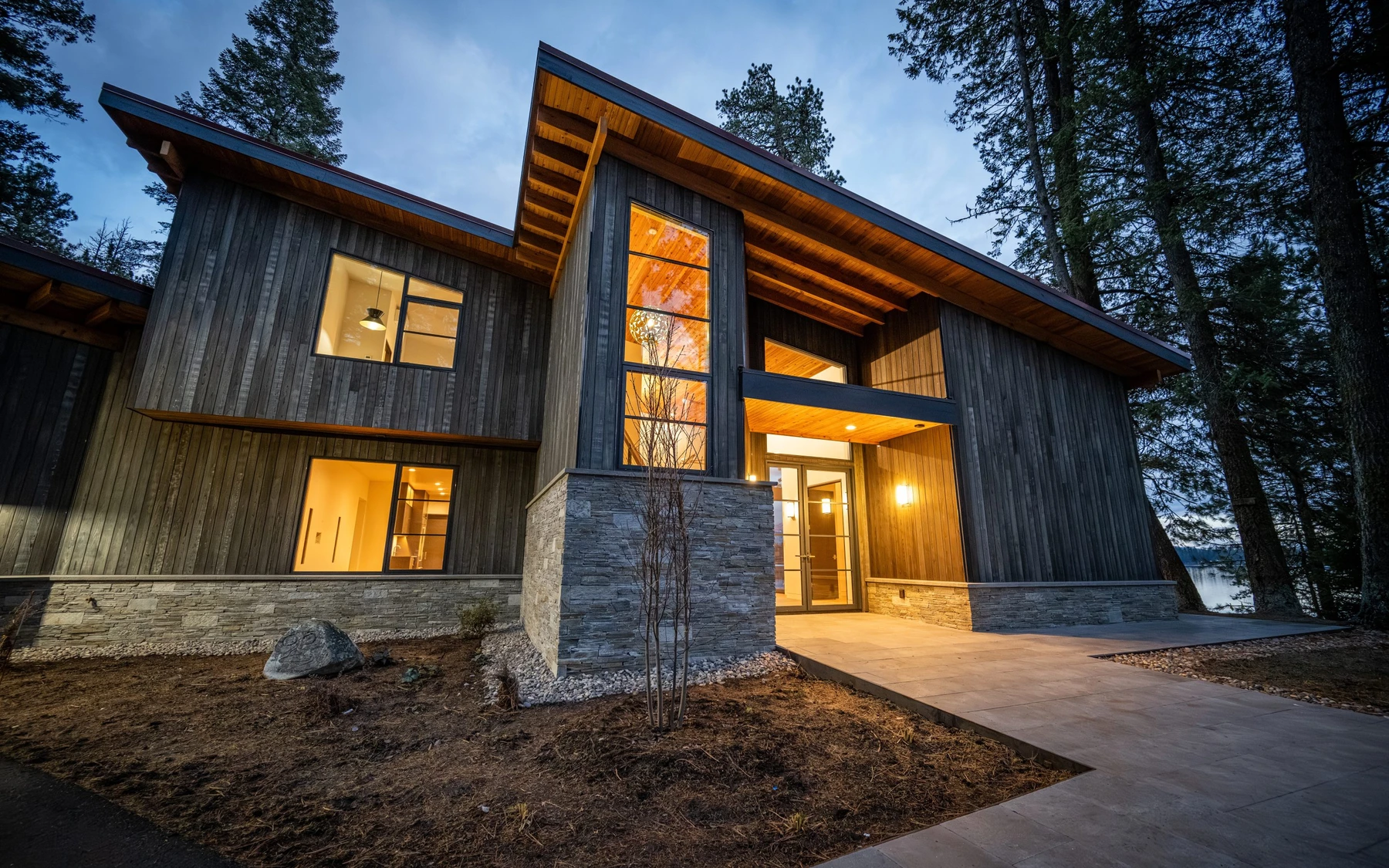 Exterior of the Modern Elegance custom home near McCall, showing wood siding and timber details, large windows, and the surrounding forest.