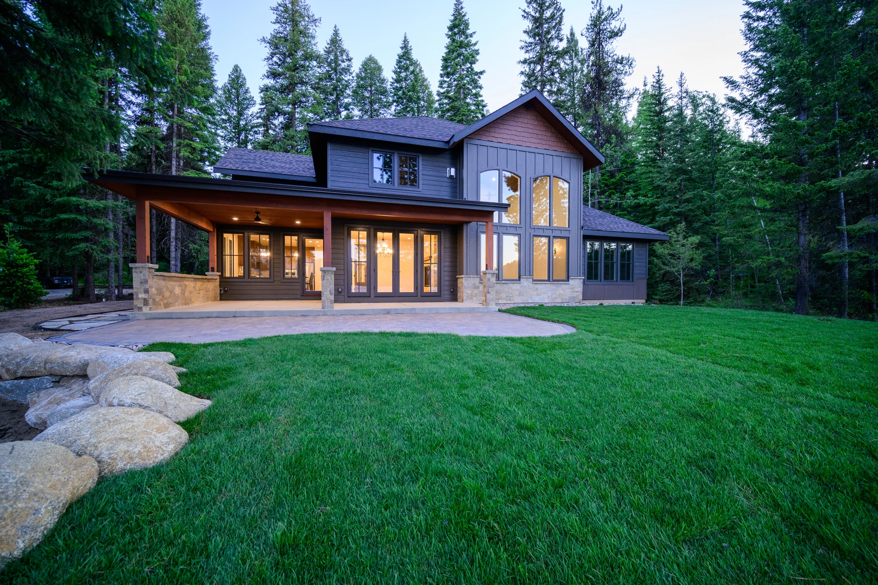 Pine Shore viewed from the lake lawn, with dark siding, warm wood accents, and tall windows among mature pines