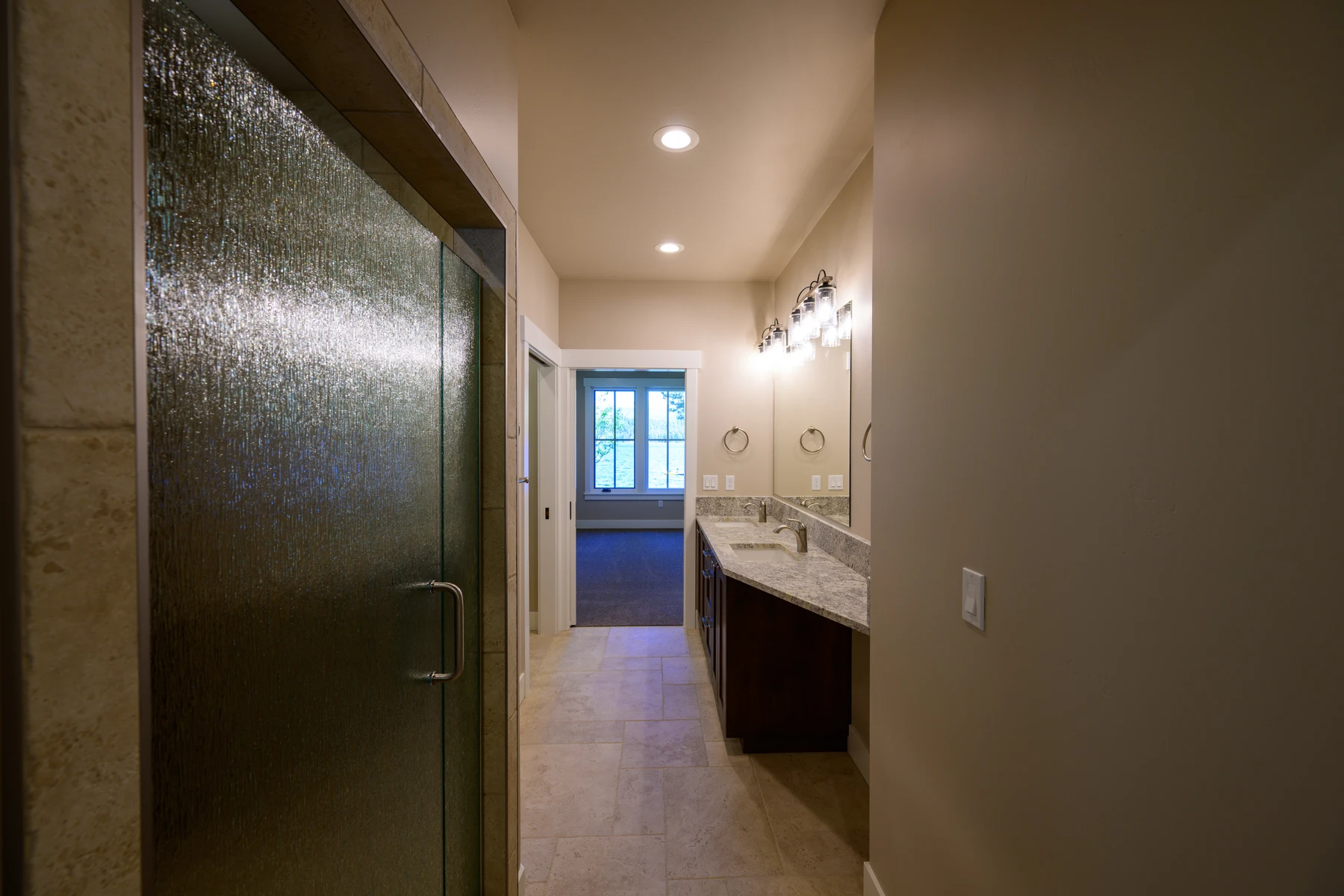 Bathroom passage with a glass shower and double wood vanity