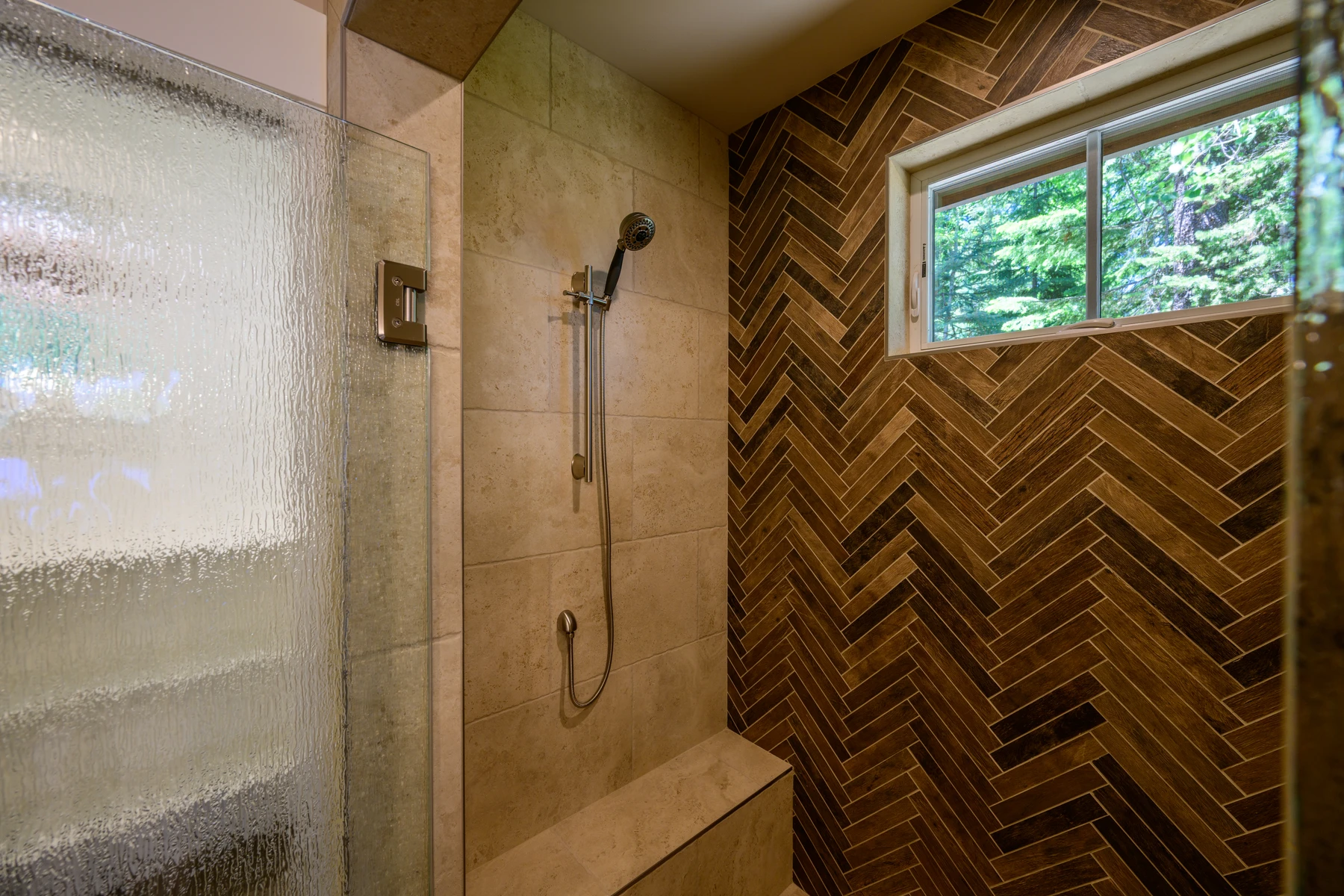Shower with a built-in bench, handheld fixture, and textured glass enclosure