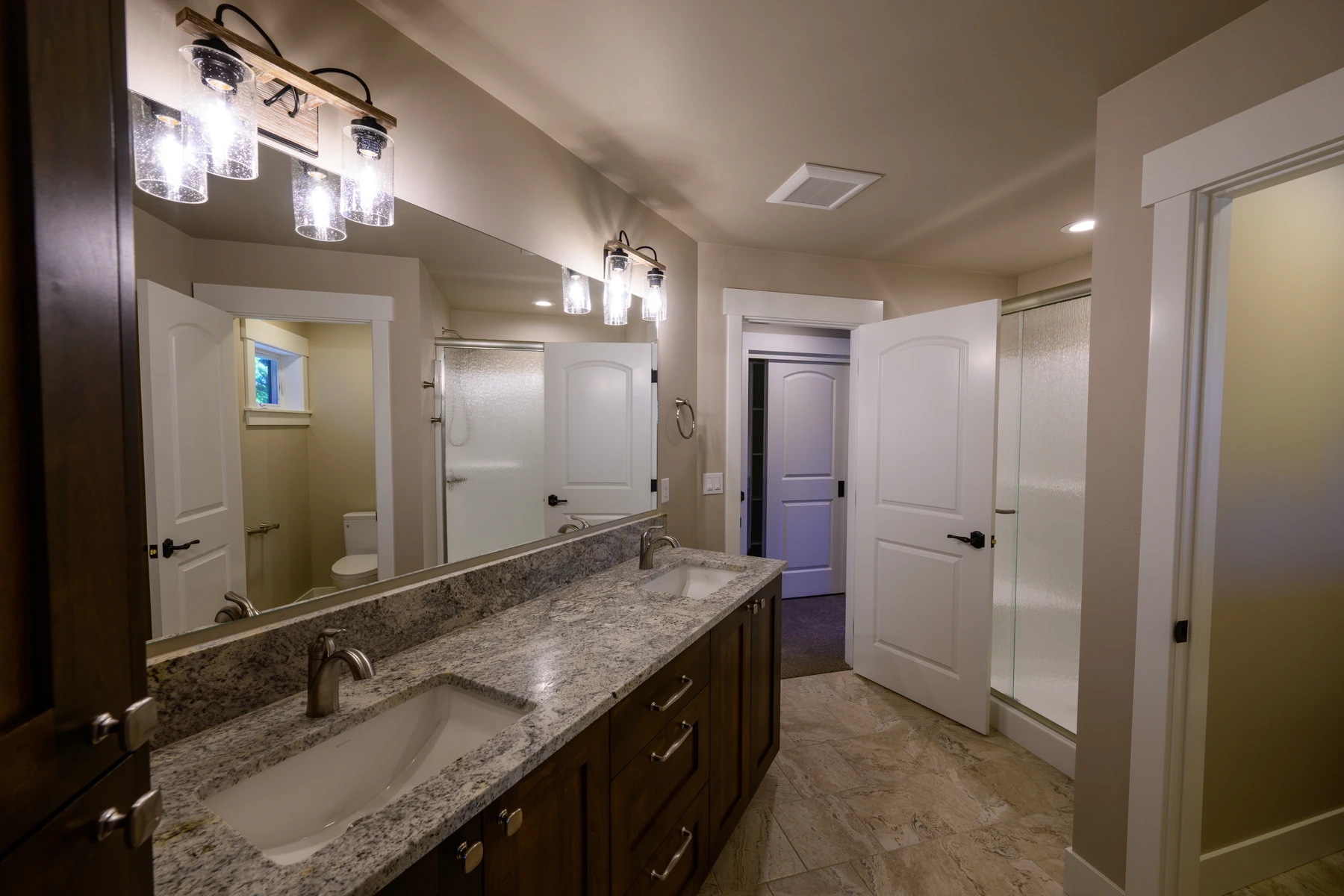 Bathroom with a double wood vanity, stone counter, and adjoining shower room