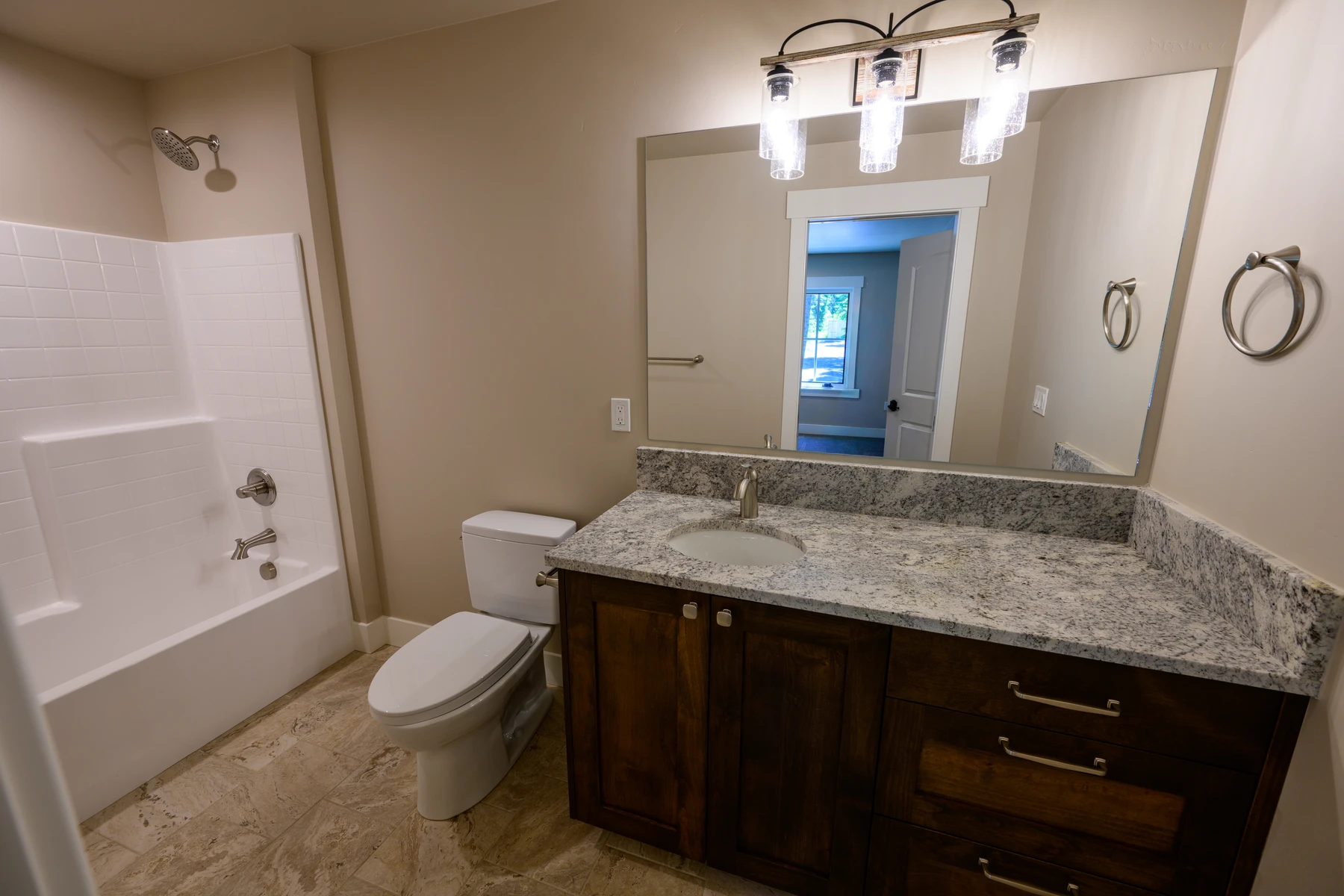 Bathroom with a wood vanity, stone counter, and tub surround