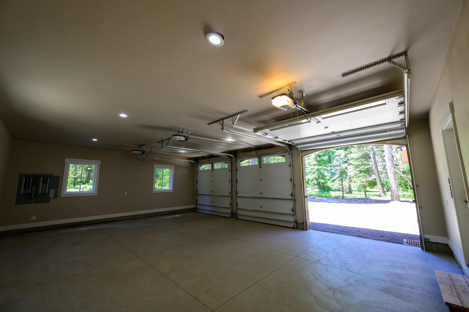 Three-bay garage with finished walls, bright lighting, and doors open to the wooded drive