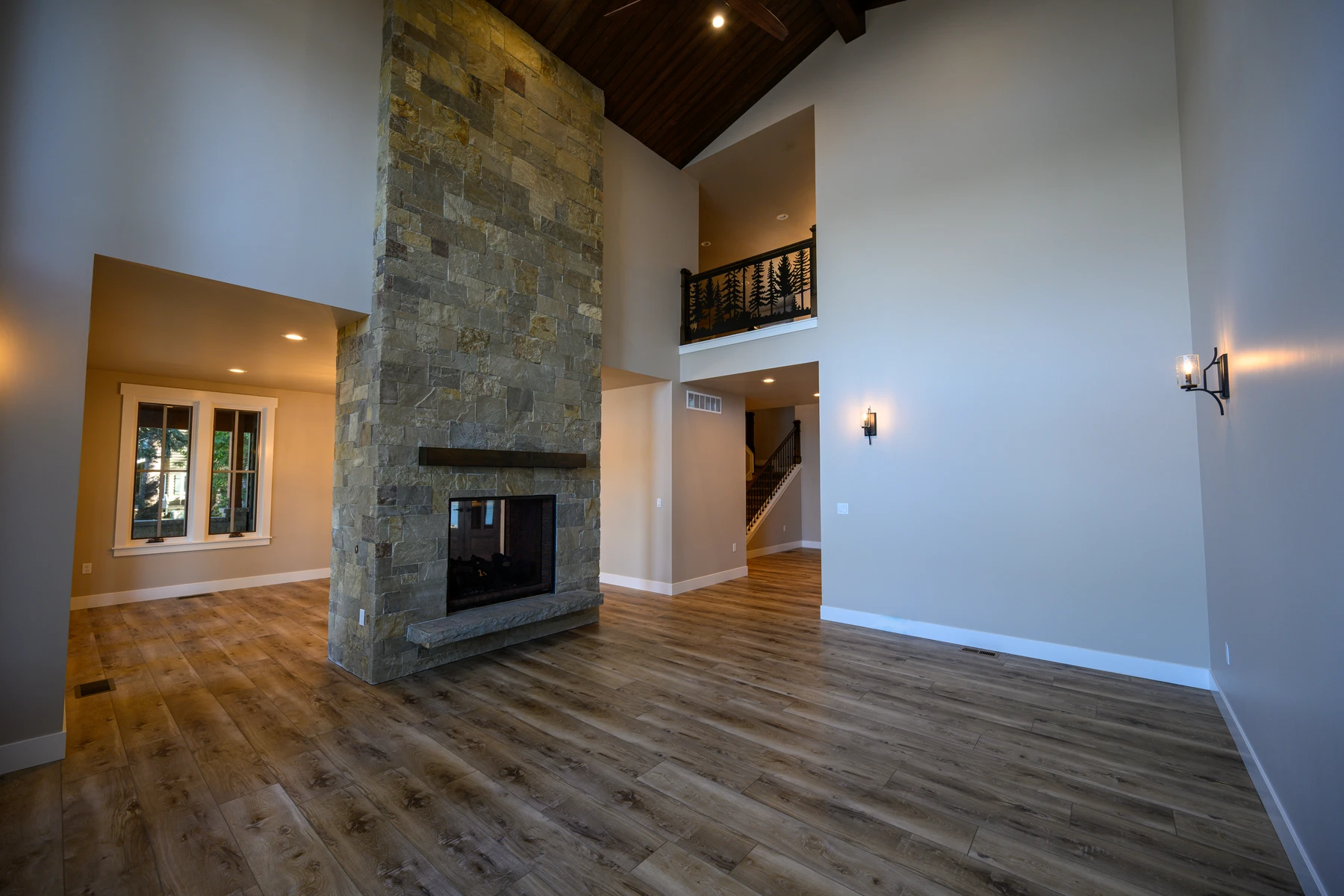 Two-story great room with a full-height stone fireplace, wood ceiling, and wide-plank floors